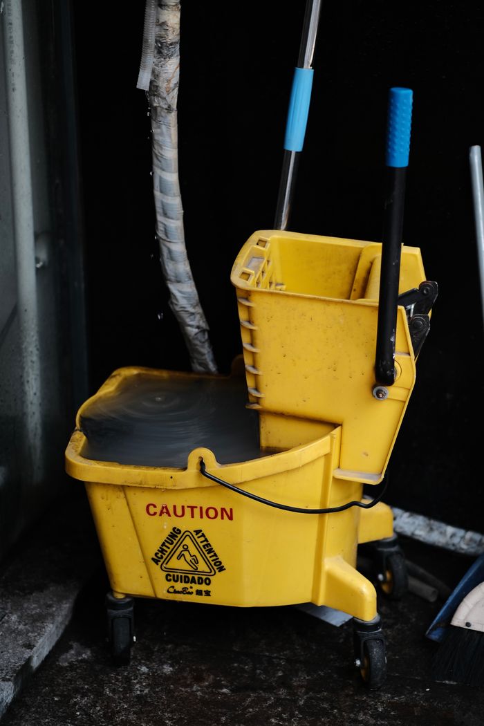 Home Close-up of a yellow mop bucket with caution sign, ideal for cleaning and maintenance themes.