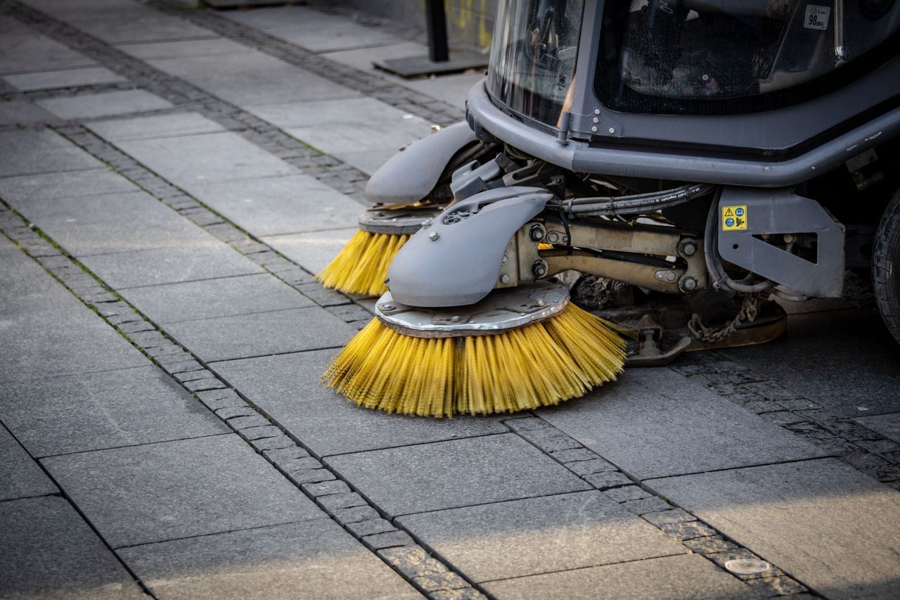 Portfolio Close-up view of a road sweeper's yellow brushes on a paved street.