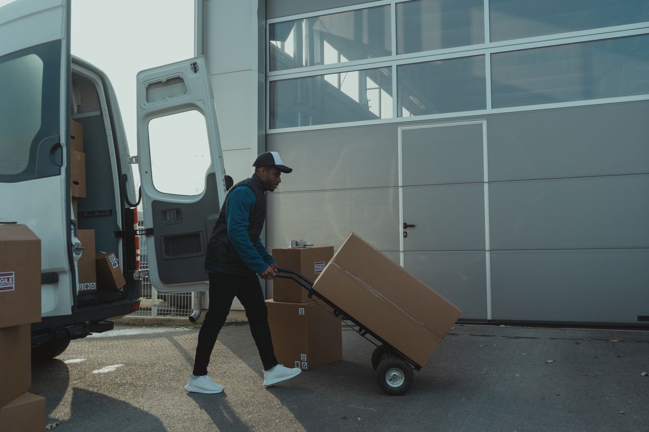 About A delivery worker with a hand trolley managing a box shipment outside a warehouse.