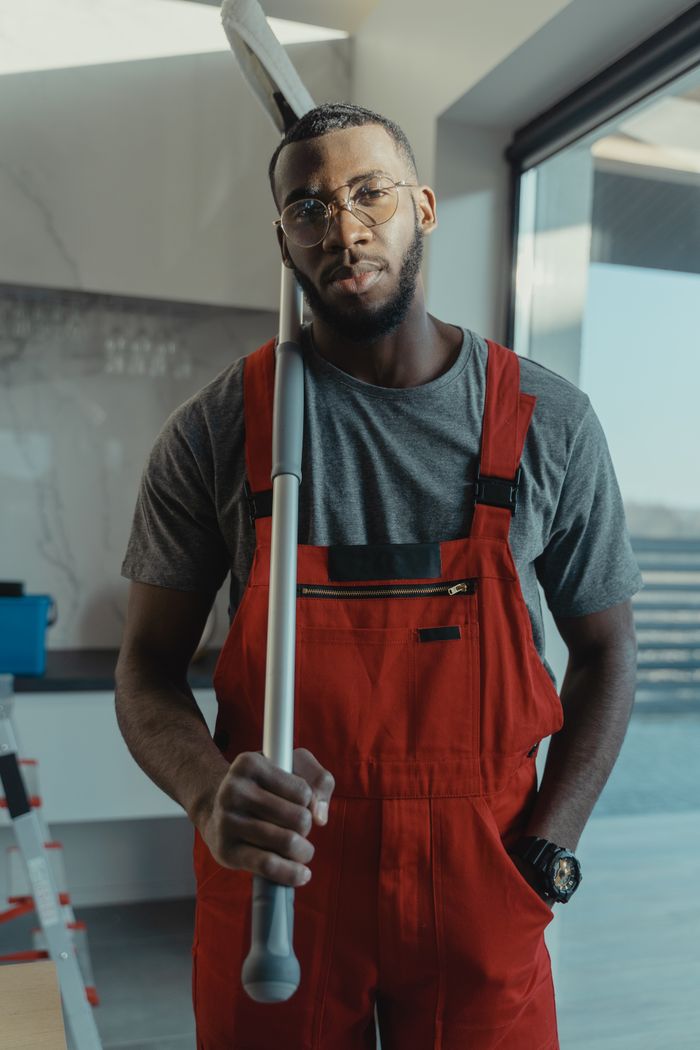 Contact Confident male cleaner posing with cleaning tool in modern interior, showcasing professionalism.