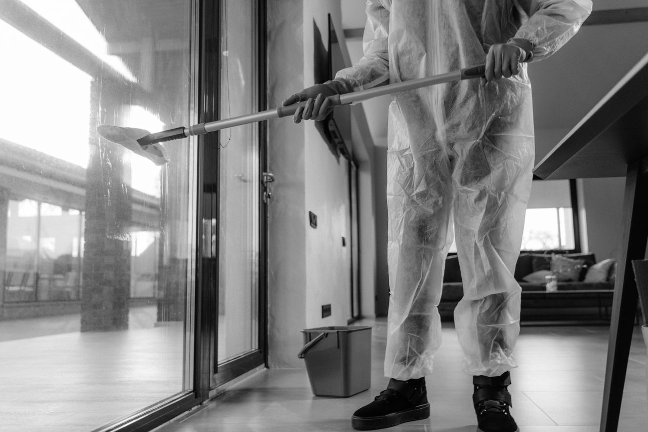 Home A person in a protective suit cleans glass doors indoors, emphasizing hygiene.
